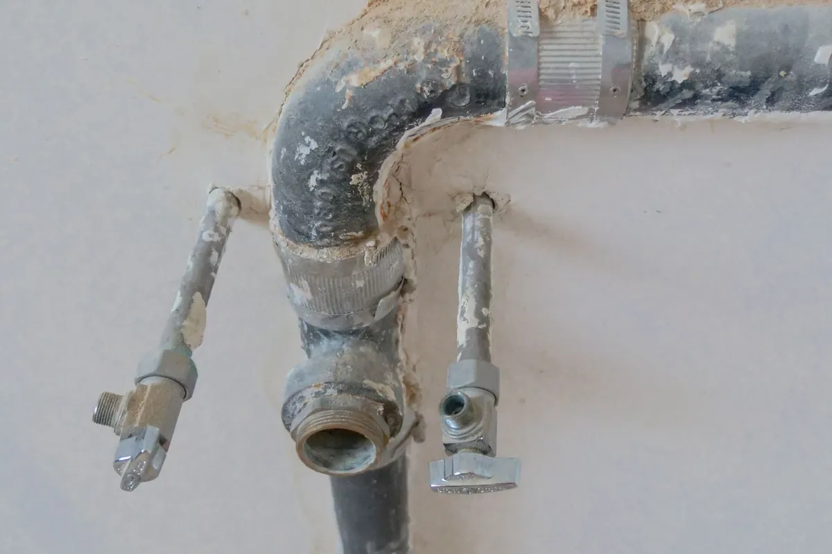 Canalisations anciennes sortant d'un mur dépiqué, avec raccords entartrés et vannes d'arrêt.
