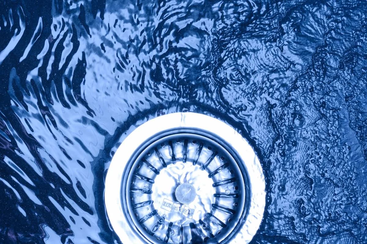 Bonde d'évier en inox vue du dessus, entourée d'eau qui stagne au lieu de s'écouler.